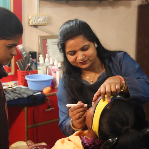 Indian woman applying make-up to customer's face